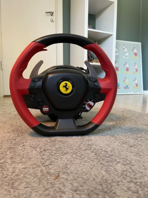 Thrustmaster Ferrari ratt USB - Säljer en Thrustmaster ratt inspirerad av Ferrari, perfekt för racing på PC eller Xbox. Ratten har en snygg röd och svart design med Ferrari-logga i mitten, paddlar i metall och flera knappar för spelkontroll. Ansluts via USB och har realistisk känsla för bilspel.