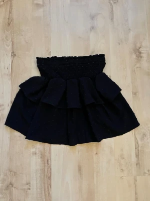 Svart volangkjol från SHEIN - Supersnygg svart kortkjol från SHEIN med bred smock i midjan och flera lager volanger som ger extra volym. Kjolen har en feminin och trendig look, perfekt att styla med en crop top eller stickad tröja. Tillverkad i ett lätt och bekvämt material.