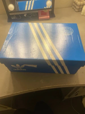 Vita Adidas sneakers med kardborre - Säljer ett par helvita Adidas sneakers med klassiska tre ränder på sidan och kardborreband över snörningen. Skorna är låga och har en stilren design i läder. Perfekta för dig som gillar en clean och sportig look. Helt nya!!!!! Kostade 1200kr
