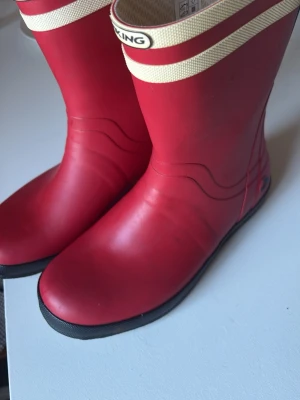 Röda gummistövlar från Viking - Snygga röda gummistövlar från Viking med vita detaljer upptill och svart sula. Klassisk hög modell i slitstarkt gummi som håller dig torr under regniga dagar. Perfekta för dig som vill ha både stil och funktion i höst och vår.