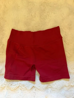 Röda  träningsshorts - Ett par helt nya röda shorts med bred ribbad midja och tight passform. Perfekta för träning eller gymmet. Materialet är stretchigt och känns mjukt mot huden. De är storlek M men passar även mig som har Xs/S då den är stretchig. Dem är aldrig använda därav inga tecken på användning . 
