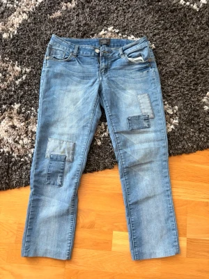Ljusblå Capri jeans från Motivi med unika detaljer  - Säljer ett par ljusblå capri jeans från Motivi med unika patchade detaljer på benen. Capri jeansen är från tidiga 2000 talet alltså vintage köpta från Italien. Strl är lite oklar men skulle passa M/L