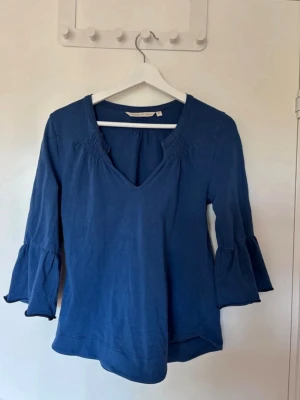 Vintage blå tröja - Blå blus med v-ringning och trekvartsärm med volang, samt har blusen smock vid axlarna.