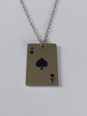 Halsband med ess i spader-hänge - Snyggt halsband med ett rektangulärt hänge i form av ett ess i spader. Hänget är i silverfärgad metall med svarta detaljer och har en stilren, modern look. Perfekt accessoar för dig som gillar kortspel eller vill sticka ut med något unikt. Materialet rostfritt stål 