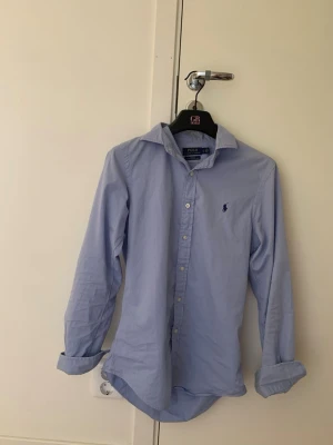 Blå Ralph lauren skjorta  - Säljer denna sjukt snygga ljusblå skjorta från Polo Ralph lauren. Perfekt nu till sommaren! I herr storlek S, jag är 180 och den passar mig perfekt. använd fåtal gånger. skriv dm för frågor! 
