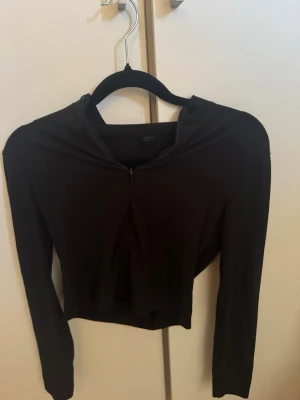 Svart croppad långärmad topp Bik Bok - Snygg svart croppad topp från Bik Bok med lång ärm och dragkedja framtill. Tillverkad i mjukt och stretchigt material som sitter skönt på kroppen. Perfekt till jeans eller kjol för en trendig look.