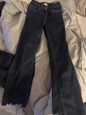 Mörkblå bootcut jeans med rå kant - Snygga mörkblå bootcut jeans med råa, fransiga benslut och kontrastsömmar. Bakfickorna har dekorativa sömmar i gult. storlek 34 från nelly passat folk som är 150cm