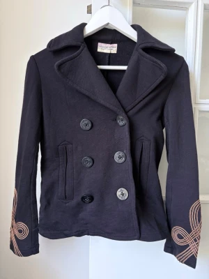 Ralph Lauren Mörkblå skepparkavaj  - Snygg mörkblå skepparkavaj från Ralph Lauren i storlek XS  med dubbelknäppning, bred krage och dekorativa broderier i koppar på ärmarna. Två fickor framtill och coola detaljer som ger jackan en unik look. Tillverkad i 100% bomull som känns bekvämt. nypris: ca 2800