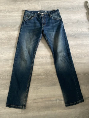 Mörkblå raka jeans från LAB Industries - Snygga mörkblå jeans från LAB Industries med raka ben och klassisk femficksmodell. Jeansen har slitningar och ljusare partier framtill och baktill för en trendig look. Tillverkade i denim med kontrastsömmar och normal midja. Storlek 170 XS HERR