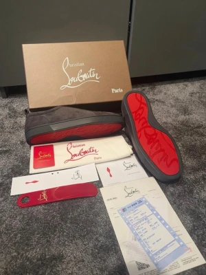 Christian Louboutin mörk grå sneakers - Mörkgrå  sneakers från Christian Louboutin med ikoniska röda sulor. Skorna har en stilren design i mocka och levereras med originalkartong, dustbag och tillbehör. Perfekta för dig som vill ha något exklusivt och trendigt i garderoben. Storlek 43! Vid frågor eller funderingar är de bara att höra av sig!