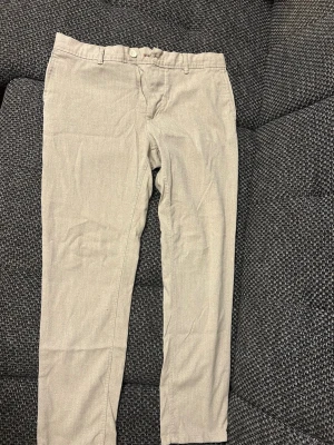 Beige chinos med dragkedja - Snygga beige chinos med klassisk passform och dragkedja framtill. Byxorna har bälteshällor och knappstängning i midjan. Perfekta för en clean och stilren look. Materialet känns mjukt och bekvämt, troligtvis bomull eller bomullsblandning.