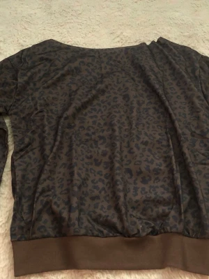 Brun leopardmönstrad hoodie - Snygg brun hoodie med leopardmönster och ribbade muddar vid ärmslut och nederkant. Hoodien har en avslappnad passform och är tillverkad i ett mjukt material som känns skönt mot huden. Perfekt för dig som gillar djurmönster och vill sticka ut lite extra.