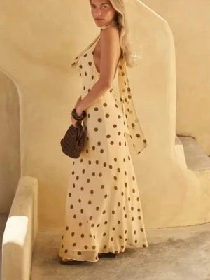 Gul långklänning med prickar - Elegant gul långklänning med bruna prickar och knytband vid axeln. Klänningen har en oneshoulder-design och är tillverkad i ett lätt, flödande material som ger en luftig känsla. Perfekt för sommarens alla tillfällen.