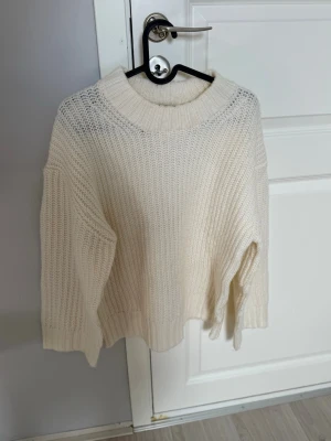 Vit oversized stickad tröja - Säljer en krämvit oversized stickad tröja med bred ribbad polokrage och långa ärmar. Tröjan har en avslappnad passform och är gjord i ett mjukt, tjockt material som känns riktigt cozy. Perfekt att slänga på sig när det är kyligt ute.