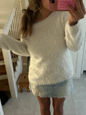 Vit fluffig stickad tröja - Mysig vit stickad tröja med fluffig textur och rund hals. Tröjan har lång ärm och en avslappnad passform som ger en trendig och bekväm look. Perfekt att matcha med jeans eller kjol för en enkel men snygg outfit. Från gina, storlek L.