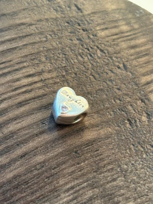 Pandora hjärtberlock i silver, med texten daughter - Säljer en söt hjärtformad berlock från Pandora i silver med texten 'Daughter' ingraverad och en liten glittrande hjärt sten på framsidan och baksidan.                              Nypris: 350kr