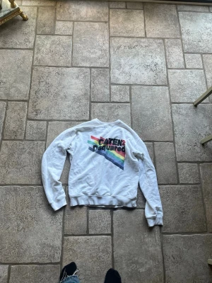 Vit Dsquared2 sweatshirt med regnbågstryck - Säljer en vit sweatshirt från Dsquared2 med färgglatt regnbågstryck och texten 'CATEN2 Dsquared' på bröstet. Tröjan har rund halsringning, långa ärmar och ribbade muddar. Perfekt för dig som gillar streetwear och vill sticka ut med en unik design.