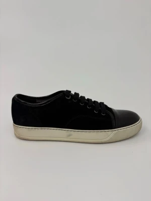 Svarta sneakers med lackdetaljer - Snygga svarta sneakers med vit sula och glansiga lackdetaljer på tån och runt snörningen. Skorna har klassisk låg profil och svarta skosnören. Perfekta för dig som gillar stilrena och moderna sneakers.