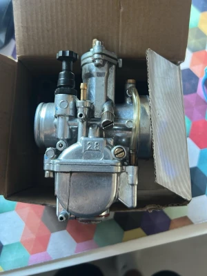 Förgasare 28mm till moped/mc - Säljer en silverfärgad förgasare i metall, 28mm, med flera justerskruvar och slanganslutningar. Passar till moped eller motorcykel. Kommer i originalkartong och har robust konstruktion med detaljer i mässing och plast.