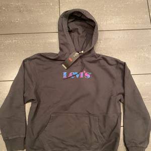 En Levis hoodie med loggan graphic och den är i färgen mörkgrå. Färgen skiftar i olika färger. Aldrig använd. Inget tecken på användning och taggen sitter kvar. Storlek M. Kan skicka mer bilder i DM. Köparen står för frakt 🚚 