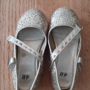 Glitter skor i stolek 27. - Guldglittriga skor andvända men bra skick. Lite små repor på klacken men inget som syns när man går.