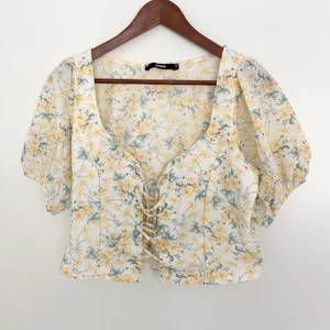 Gul blommig topp med snörning  - En gul blommig topp med snörning fram från BikBok i storlek M som jag antar är slutsåld ✨  Säljer pga att den är för stor för mig och att den aldrig har blivit använd ✨  Nypris: kommer ej ihåg men under 150kr ✨  För fler bilder och frågor så är det bara att meddela mig ✨  Toppen är ljusare än vad den är på bild