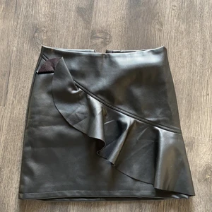 En skinnkjol i storlek 146/152 - En kort skinnkjol som är oanvänd, bra kvalitet med en volang på framsidan, och även en dragkedja på rumpan. 