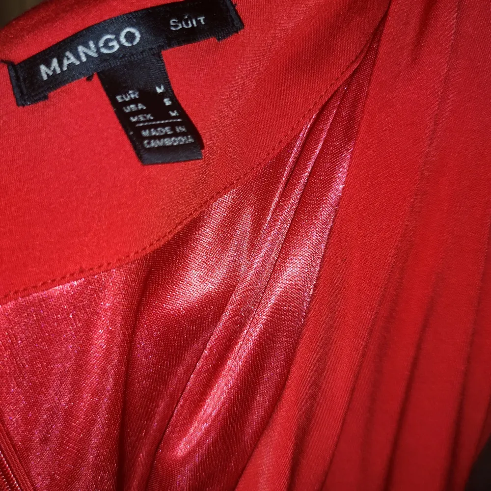 En röd klänning från Mango Suit kollektion. Väldigt klarröd, mjukt och lyxigt tyg/underklänning insydd i. Väldigt urringad (observa att en ser min mjuka bh i bild. Dragkedja bak samt en hake längst upp. Lätt att knäppa själv tycker jag. Drapering i midjan och tight runt höfter och rumpa. Djup v-ringning. En small men tror en medium kan ha den också. Använd en gång. Jättefint skick. Säljer för att den inte helt passar mig.. Klänningar.
