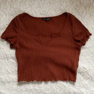 En brun, ribbad T-shirt från Shein. Vid nederdelen på tröjan och även vid ärmarnas slut är det som små volanger och vid halsen är det som en liten slits.