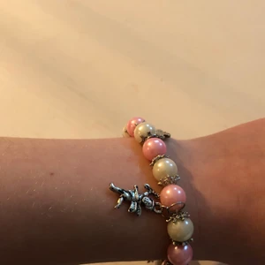 Rosa/vitt armband med små figurer - Det är ett armband med små änglar och andra figurer på. Skicket är ok figurerna har tappat lite av silver färgen på vissa ställen. Knappt använt. 