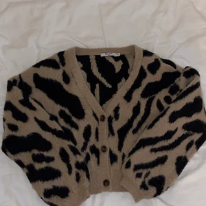 Mönstrad stickad kofta - Beige och svart stickad kofta som går till naveln och sitter ganska tajt på kroppen om den är knäppt.