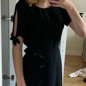 Festlig svart klänning  - Svart klänning som passar perfekt till fest med knyte i midijan och detalj med knyte på armen. Inte använd mycket. Klänningen går till knäna typ. Skriv om mer bilder.