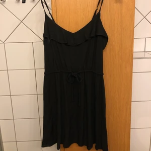 Svart klänning strl 34 - En svart supergullig, kort, sommarklänning med fina volanger, knytning i midjan och justerbara axelband. Klänningen är i fint skick. 