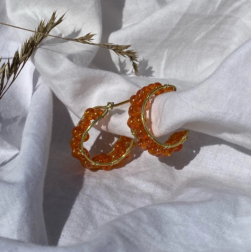 Handgjorda örhängen med orangea pärlor, och guldpläterad koppartråd. Nickel-, kadium-, och blyfria. OBS! Kommer utan plupp att sätta på baksidan.  2,5 cm i diameter. Accessoarer.