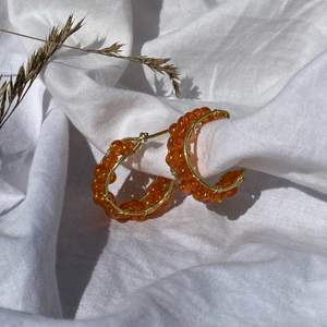 Handgjorda örhängen med orangea pärlor, och guldpläterad koppartråd. Nickel-, kadium-, och blyfria. OBS! Kommer utan plupp att sätta på baksidan.  2,5 cm i diameter