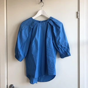 Blå blus med puffärm. - Blå blusmed puffärm. Dragkedja bak. H&M. Stlk 38. 100% bomull. Tvättas 40 gr.