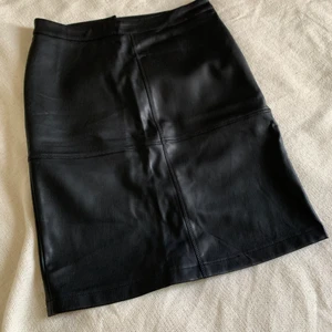 Svart pennkjol i fuskläder - Svart pennkjol i fuskläder med dragkedja bak samt sydda detaljer på fram och baksida. Slits bak vid låren.