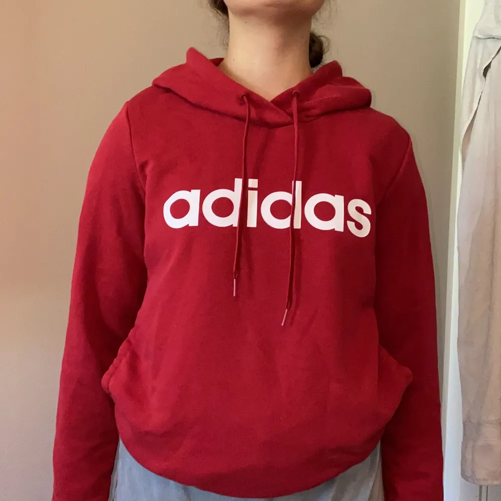 Vinröd Adidas hoodie med en ficka vid magen. Modellen är 160. . Hoodies.