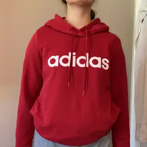 Vinröd Adidas hoodie med en ficka vid magen. Modellen är 160. 