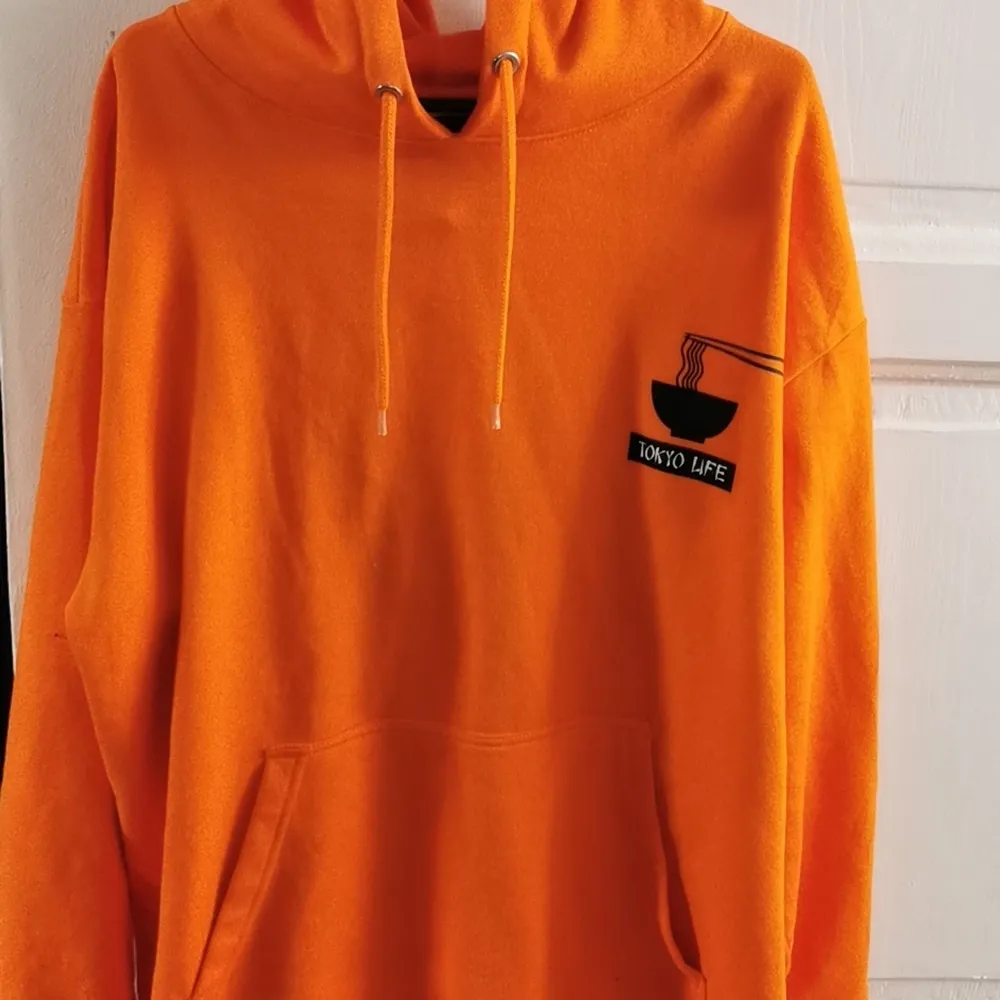 Här har vi en orange hoodie med ett tryck där det står 