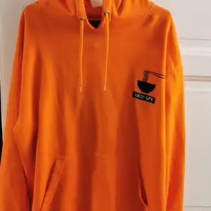 Här har vi en orange hoodie med ett tryck där det står 