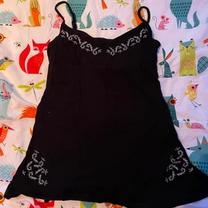 Svart linne med mönster - Ett sånt coolt svart linne med vida broderade mönster vid bysten och nere vid höften, har alldelles för många linnen så gör mig av med några!