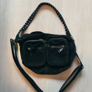 Noella väska svart - Rymlig fin väska från Noella, knappt använd.                   Har två band, ett kort med nitar och ett längre justerbart crossbody-band. Köparen betalar frakt.                                          Nypris 700kr, men säljer för 150kr