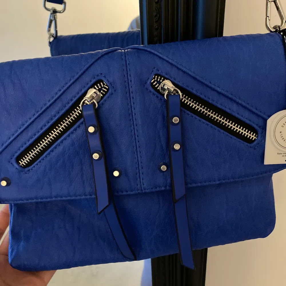 Säljer min Donna Donna väska som aldrig är använda och prislappen är kvar. Den blåa färgen är otroligt snygg och passar perfekt nu till sommaren. Det tjocka bandet gör väskan extra snygg och detaljerna. Väskan kostade 400kr.  Man kan självklart byta ut bandet också.🤩. Väskor.