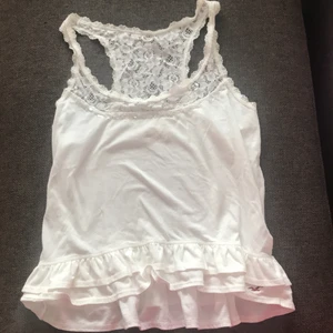 Vitt Hollister linne  - Vitt hollister linne med spets, volang och paljetter. Endast använd ett fåtal gånger. (Skrynklig Pga flytt)storlek M men passar även S 