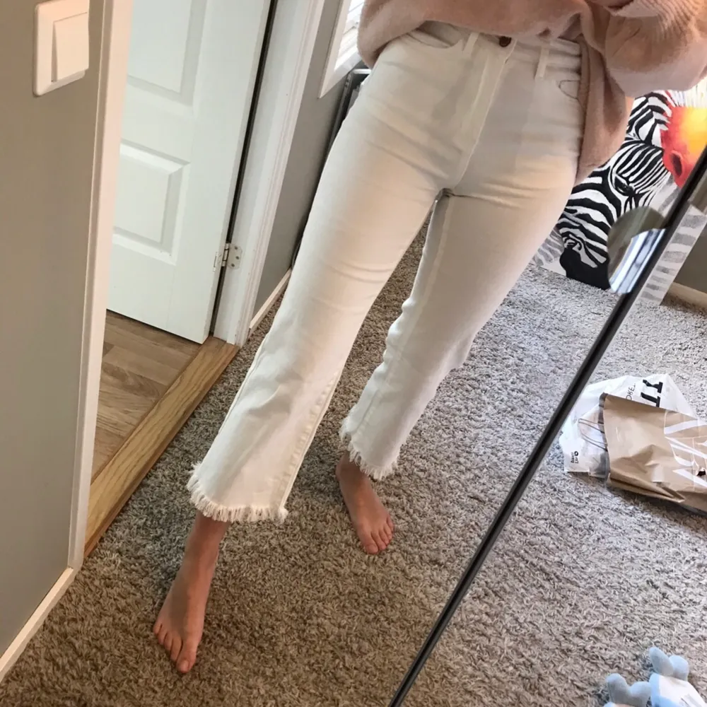 Ett par vita jeans med fransar av trådar längst ner. Jeansen har hög midja, en lite vidare passform och är i storlek 34.. Klänningar.