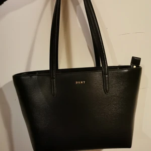 DKNY VÄSKA  - Nypris: 2275:-   Färg: svart Material: Syntetiskt material, Kohud Mått (B x H x D): 39,3 cm x 24,1 cm x 10,7 cm (mätt på väskans undersida) Max bredd: 41 cm Vikt: 687 g