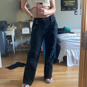 Svarta byxor med detaljer  - Säljer dessa snygga svarta byxor med coola detaljer! Jag är ca 170cm, de sitter lite stort i midjan på mig men funkar bra med skärp!