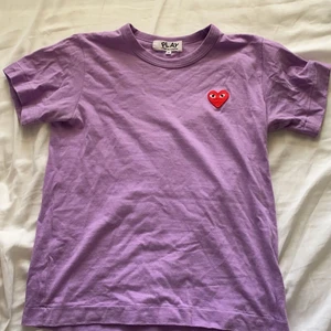 Cdg tröja lila - En lila t-shirt från Cdg med ett rött hjärta. Köpt på nk, nypris 999 kr men köpte den på rea för 699 kr. Väldigt bra skick, dock ganska liten i storlek för att vara en M. 