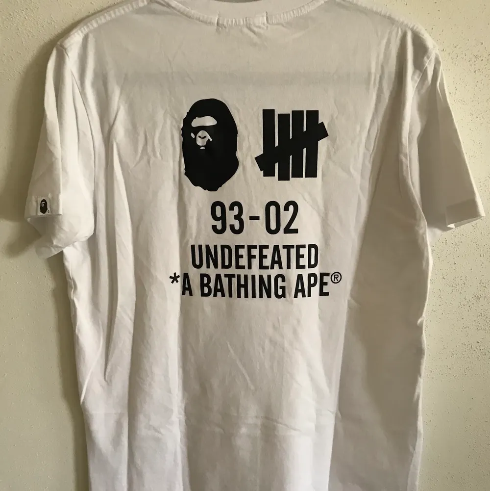 Bape / A Bathing Ape x Undefeated Velcro Logo T-Shirt  Size large, fits like a regular men’s medium. Great condition, no flaws or damage.  DM if you need exact size measurements.   Buyer pays for all shipping costs. All items sent with tracking number.   No swaps, no trades, no offers. . T-shirts.